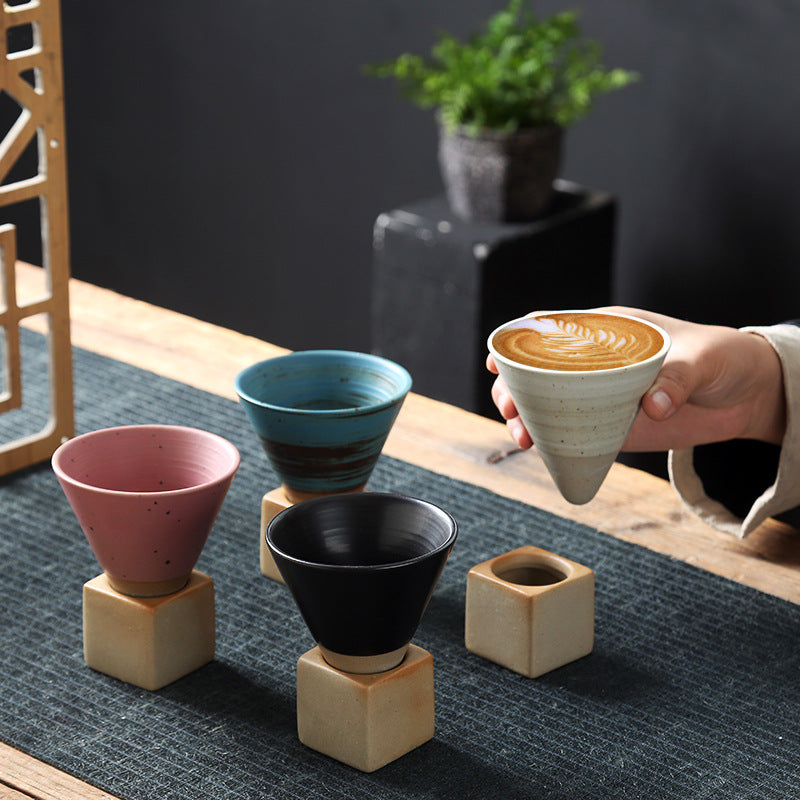A hand lifting a white cup with latte art from a row of espresso cups on their bases