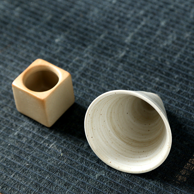 The cube base with its round recess next to the cup lying on its side, showing the interior
